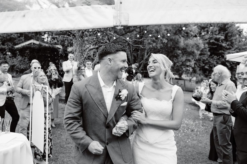 Black and white photo of a joyful bride and groom walking together at an outdoor wedding reception.