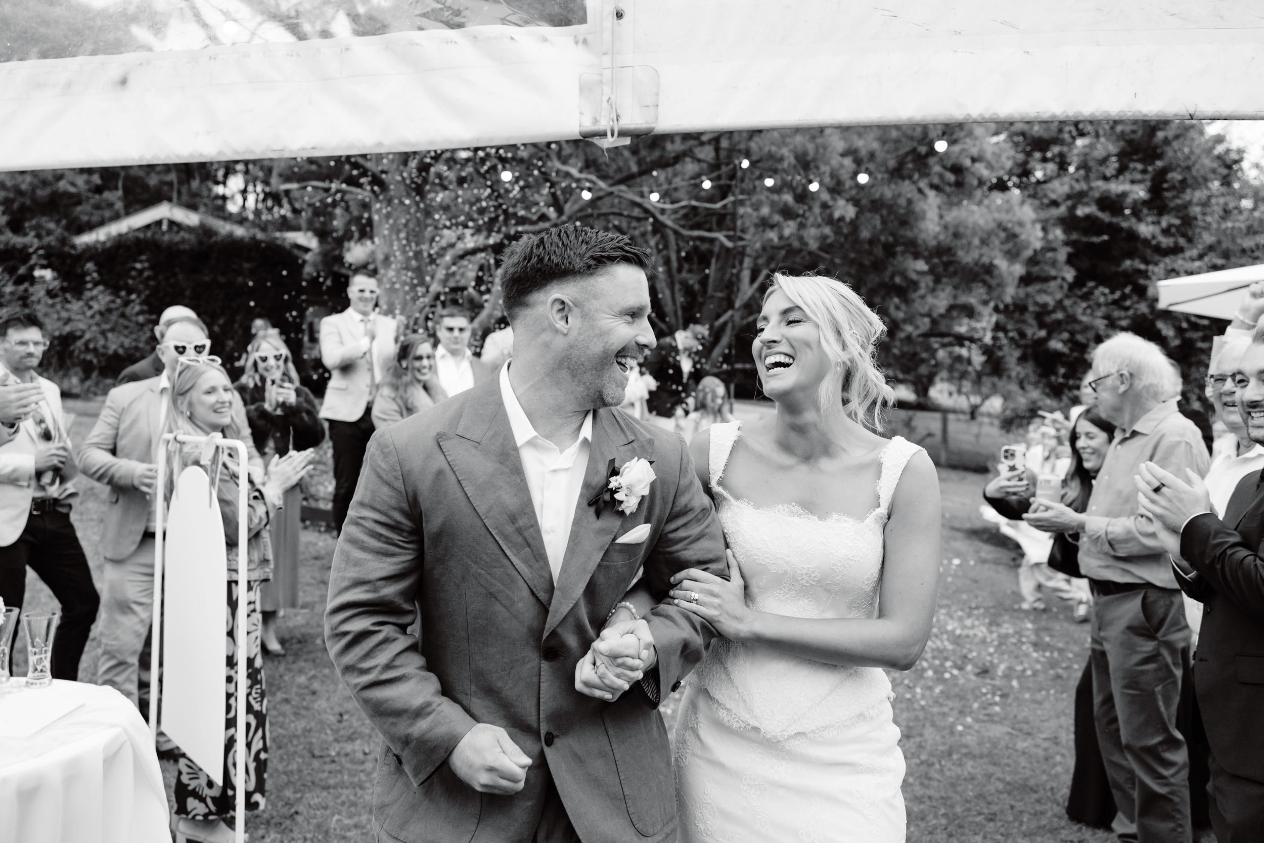 Black and white photo of a joyful bride and groom walking together at an outdoor wedding reception.