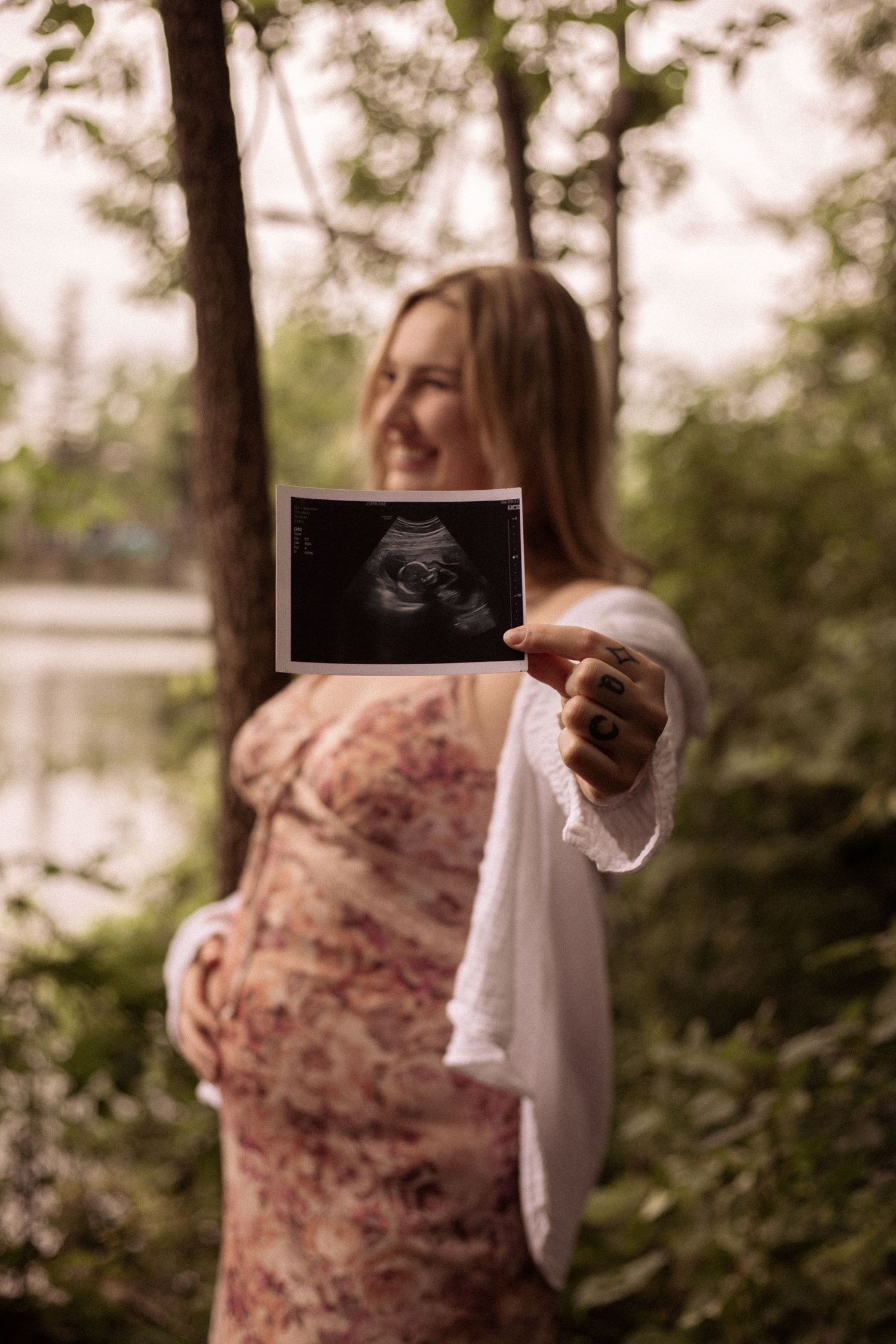 A woman excited to welcome her new baby holds up her ultrasound photo to show off her little one while smiling in the background
