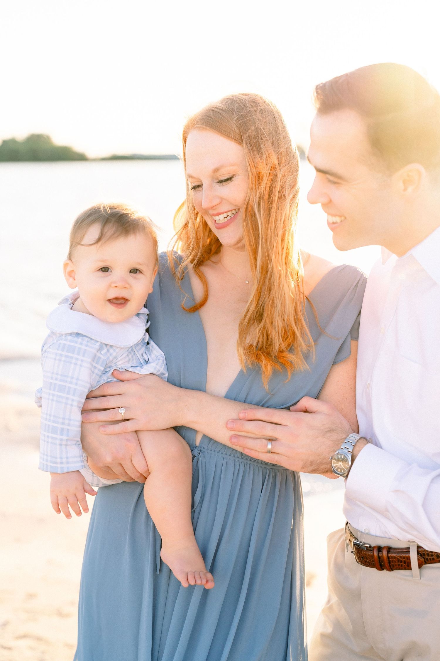 mom and dad holding hands during their maternity session on the beach at golden hour in st. Pete while the pregnant belly is in focus