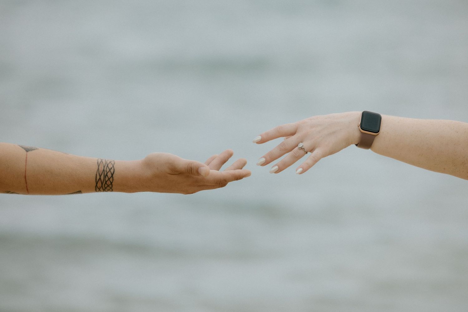 Two hands reach toward each other against a gray ocean backdrop.