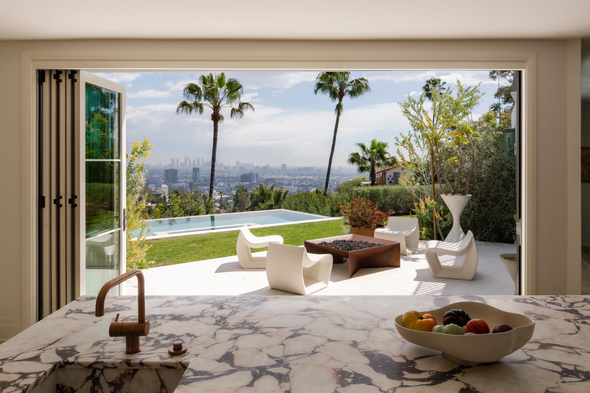 Luxurious indoor-outdoor space with marble table overlooking city views and infinity pool.