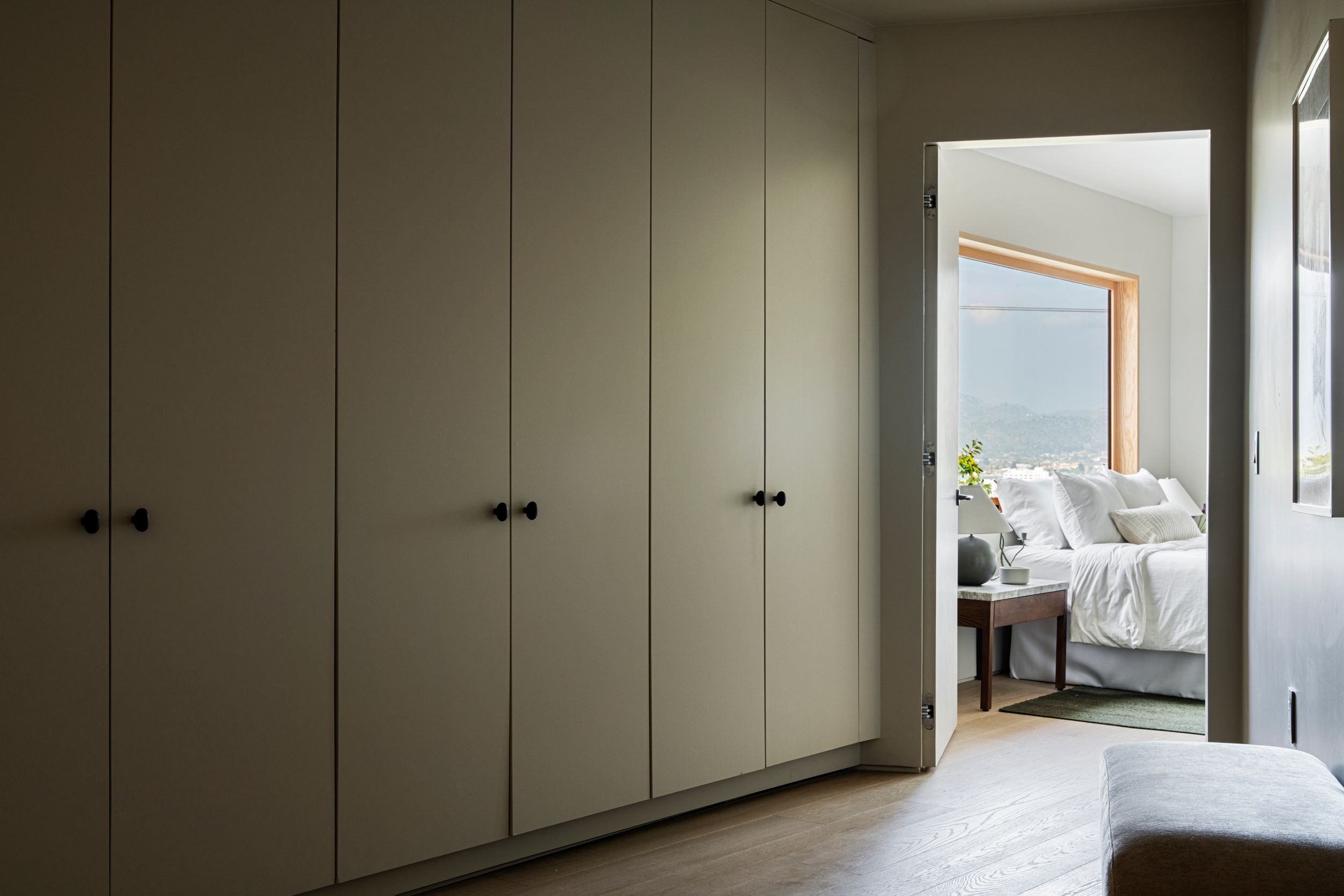 Built-in white wardrobes line a hallway leading to a bright bedroom glimpsed through an open doorway.