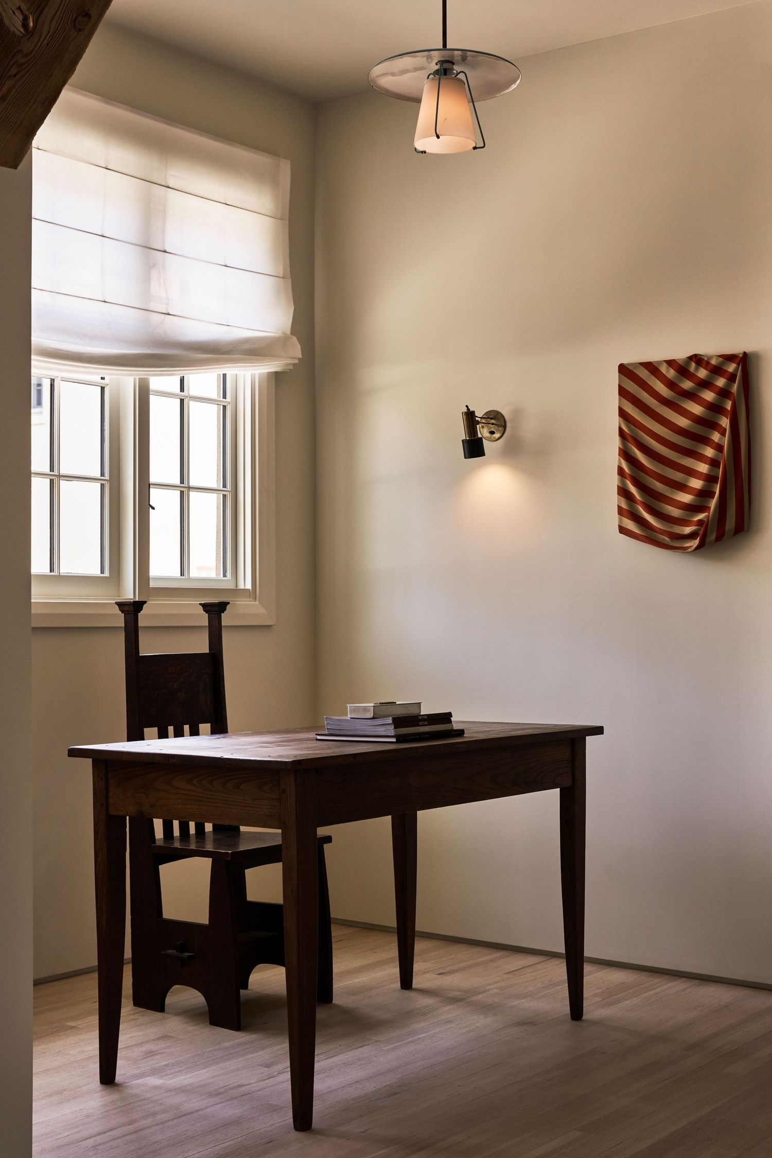 Minimalist interior space with dark wooden table and chair against white walls and natural lighting from windows.