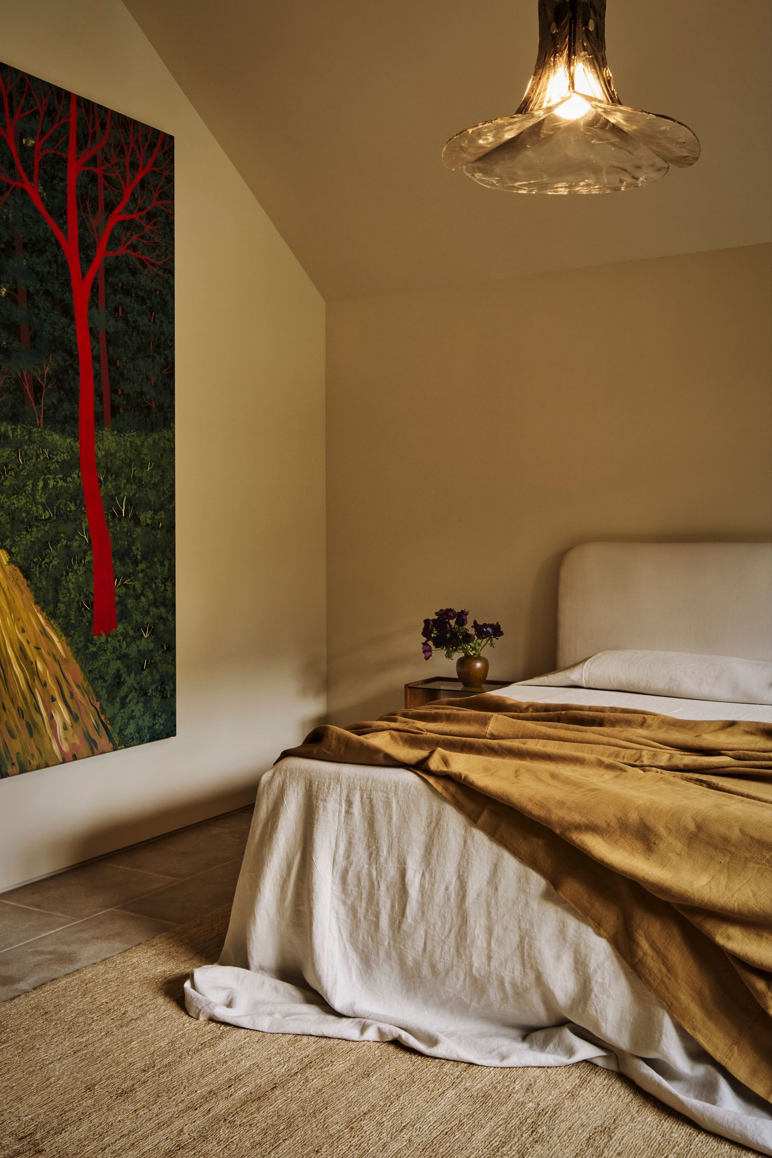 A series of bedroom photos showing an unmade bed with gold bedding and white sheets against a wall with red tree artwork.