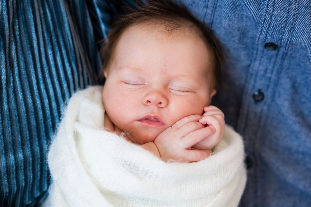 Peaceful sleeping newborn baby wrapped in soft white blanket against blue background.