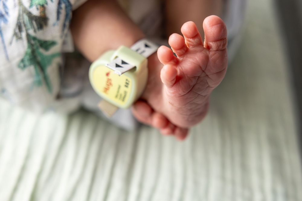 A tiny baby foot with hospital ID bracelet rests on white bedding in a close-up view.
