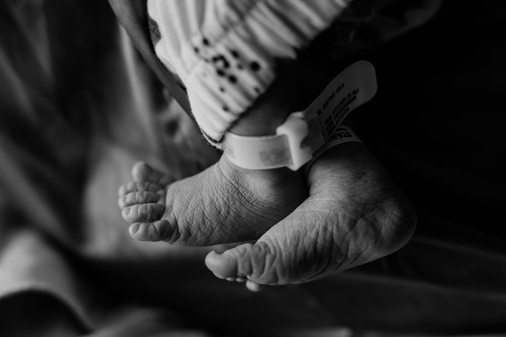 A black and white closeup photograph of a newborn baby's tiny feet against a dark background.