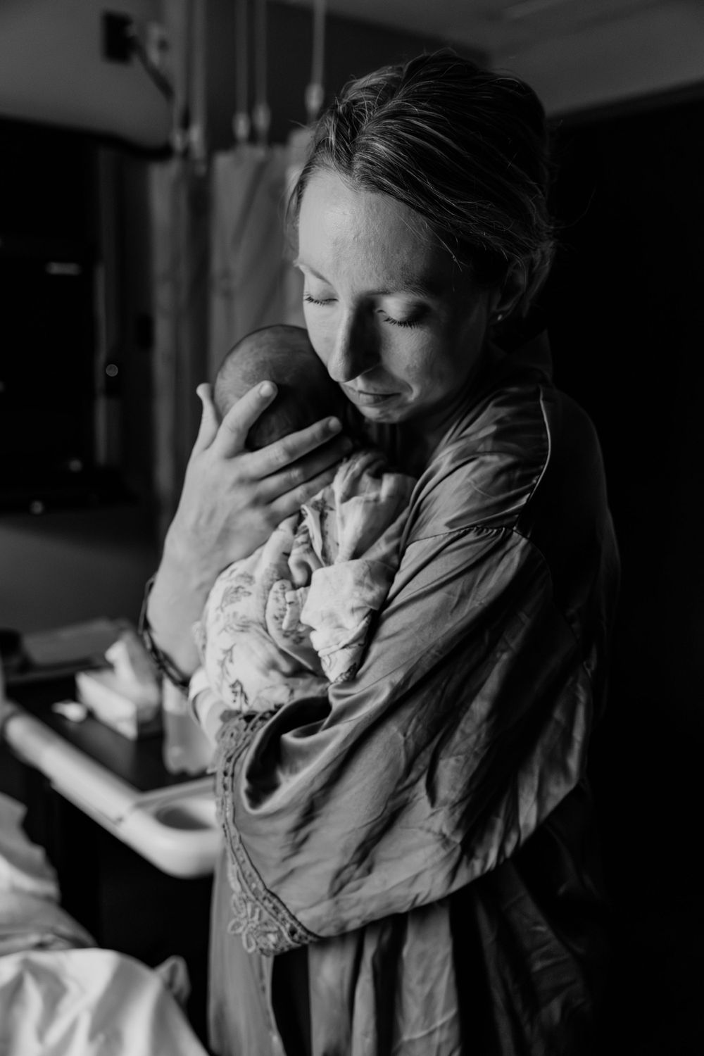 A tender black and white moment as a parent cradles their newborn baby in a dimly lit room.