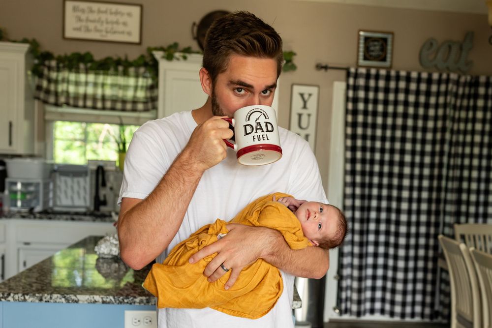 A cozy kitchen scene with someone drinking from a "Dad" mug while cradling a caramel-colored cat.