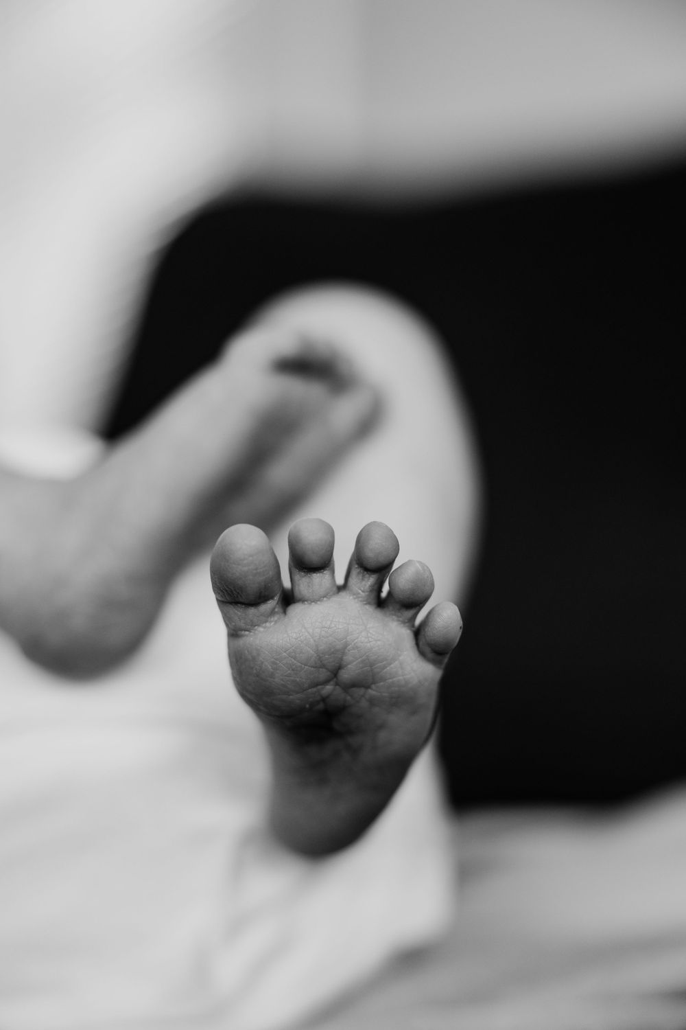 Close up black and white photo of tiny baby foot with curled toes against white background.