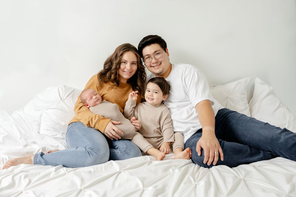 Family of three relaxing together on white bedding wearing casual clothes in a bright room.