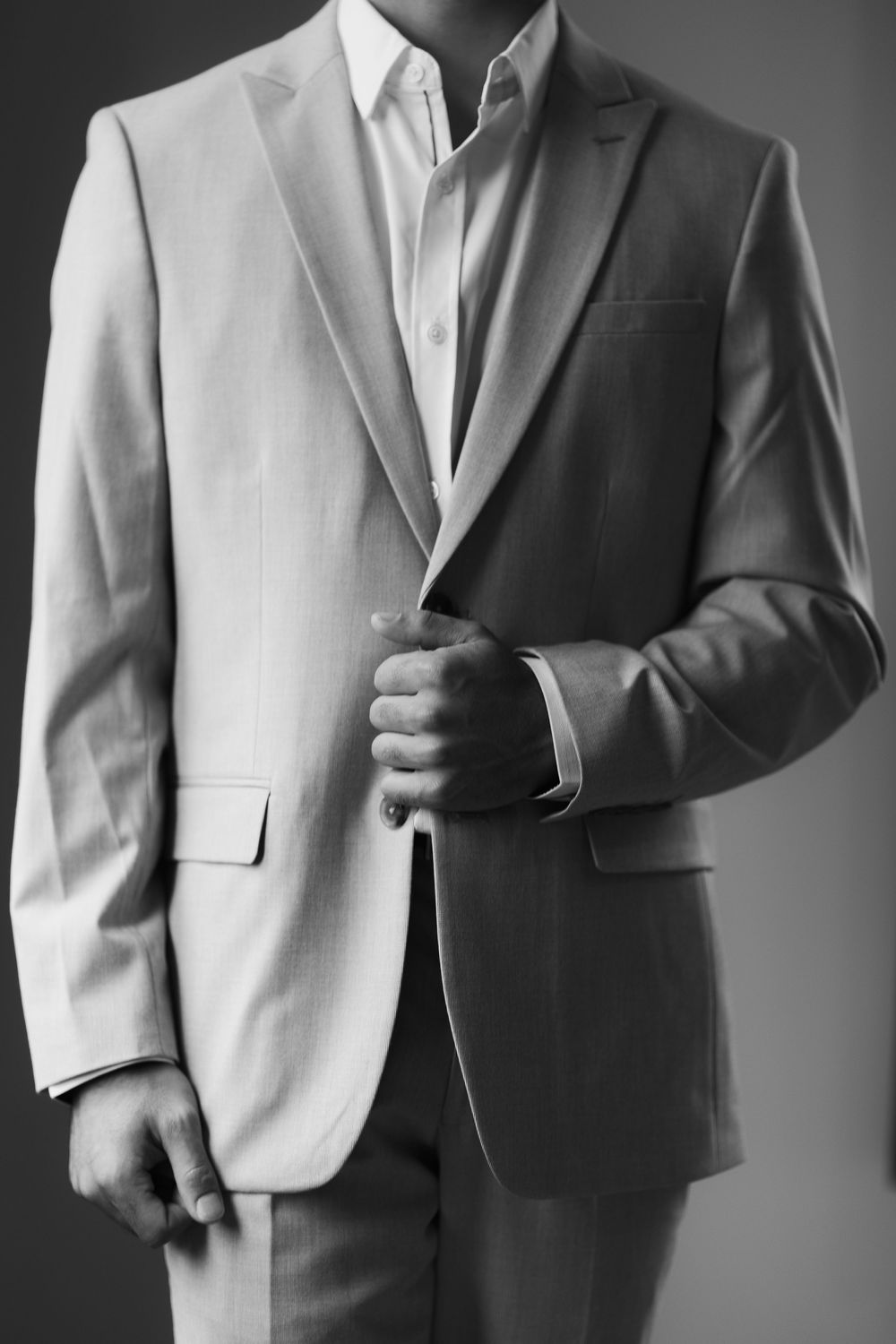 Black and white photo of a man in a tailored suit jacket, adjusting his cuffs, showcasing elegant formal menswear.