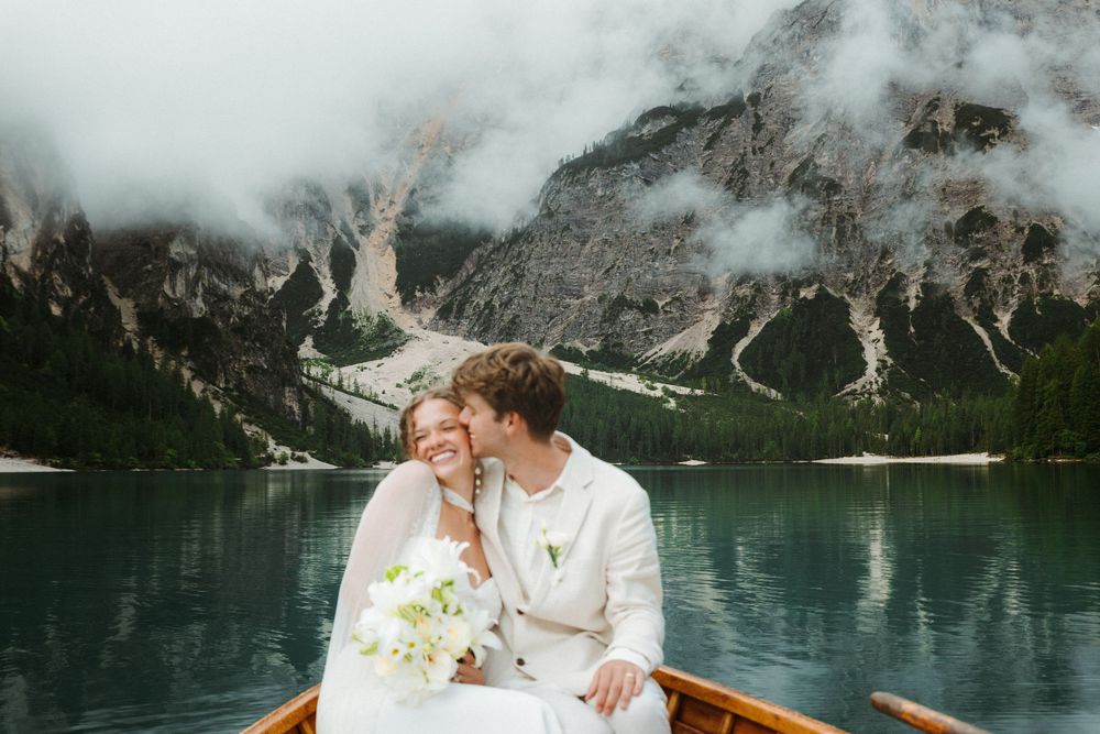 A couple in wedding attire shares a romantic moment while boating on a turquoise alpine lake surrounded by mountains.