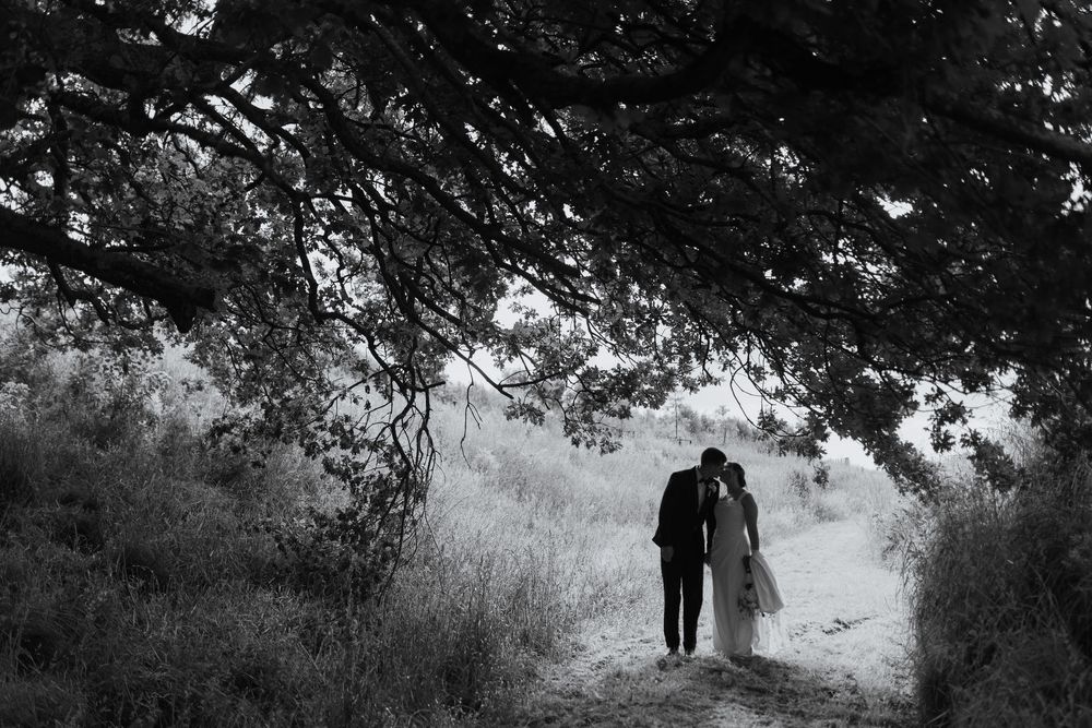 Black and white photo of a couple walking hand in hand on a path under a large tree.
