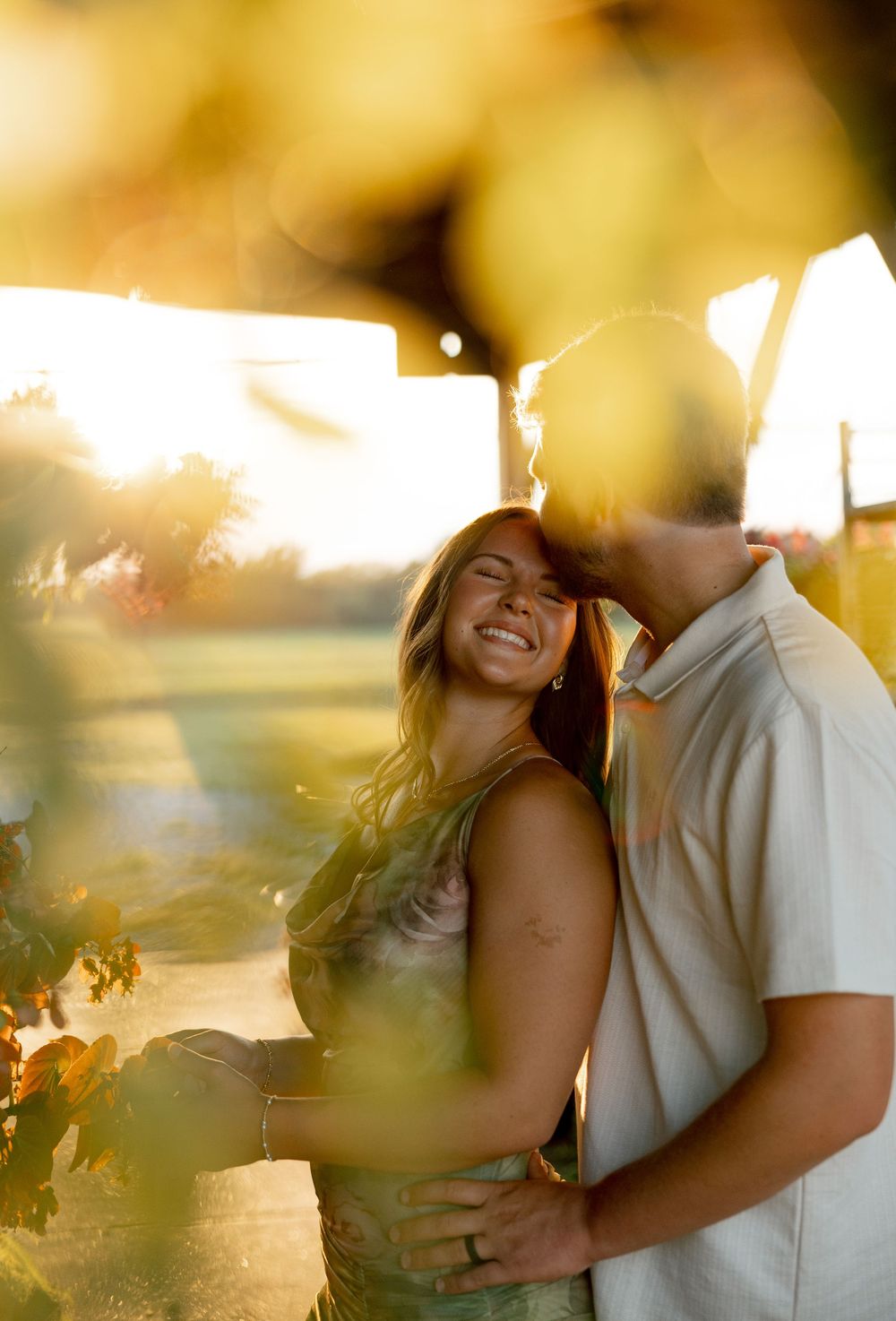 A romantic couple embraces in warm golden sunlight during a sunset photoshoot outdoors.