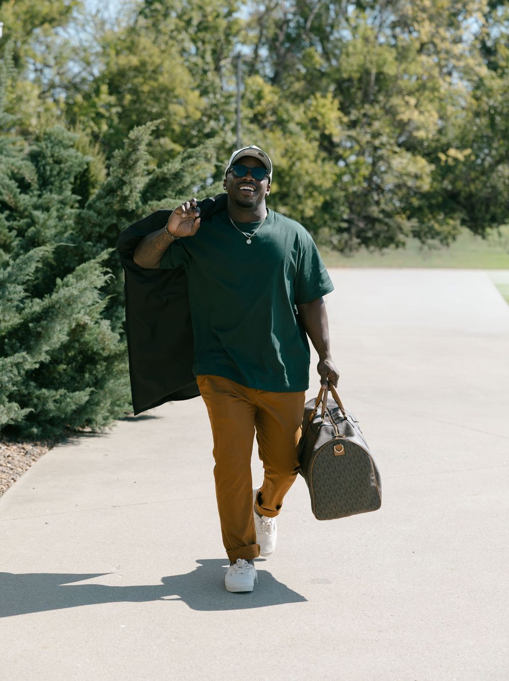 A person in a dark green polo and khaki pants walks along a path carrying a duffle bag.