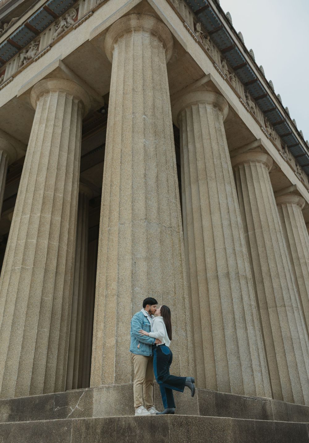 A couple shares a romantic moment between towering classical stone columns in a series of progressive shots.