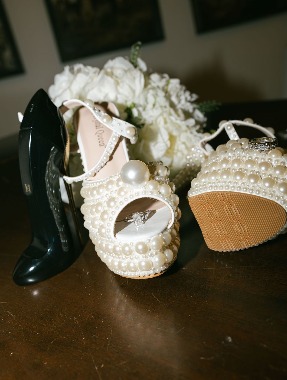 Wedding shoes displayed on dark wooden surface showing elegant white pearl-decorated bridal heels and black formal shoes.