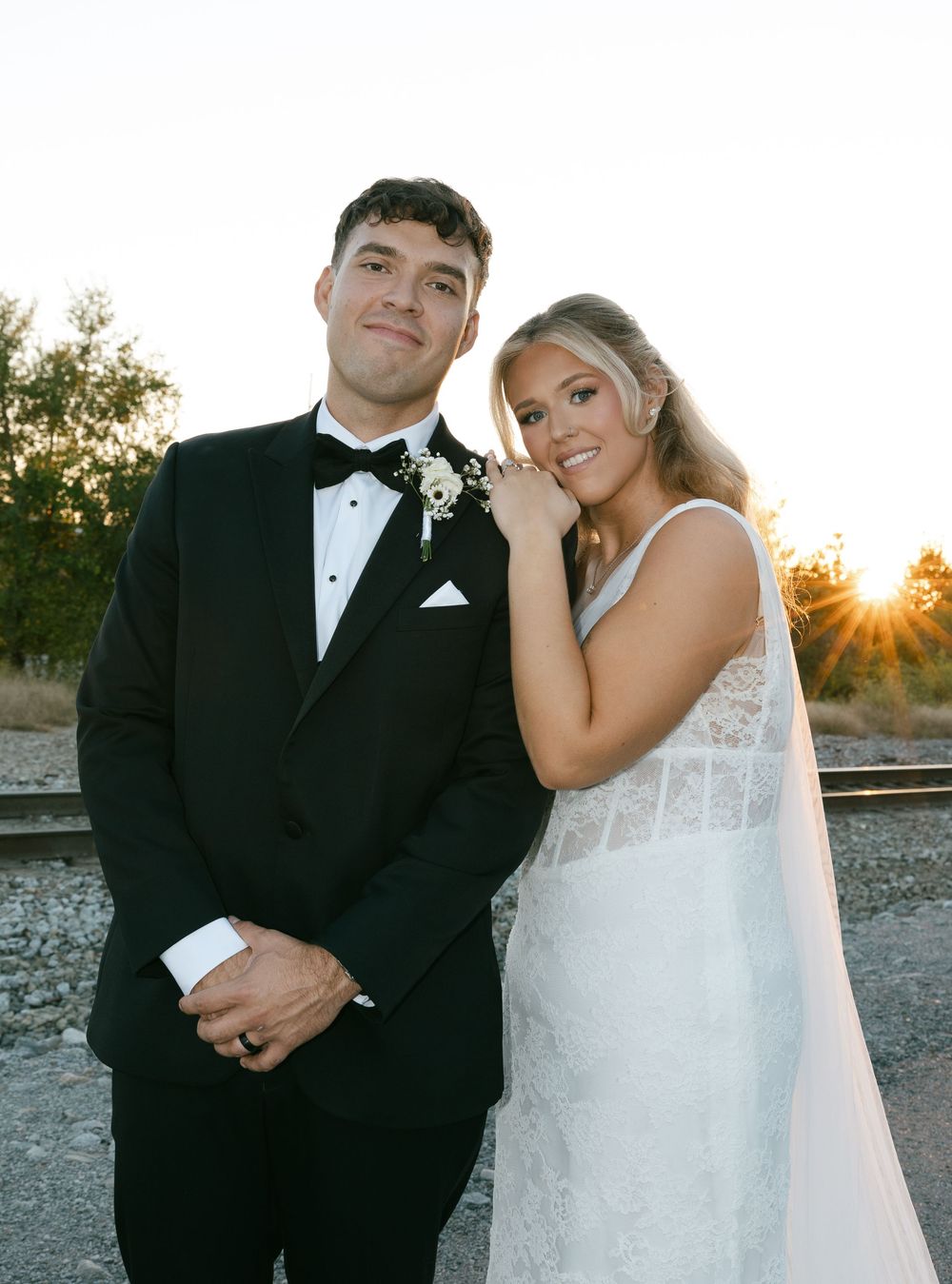 Wedding couple poses outdoors at sunset with desert landscape and dramatic lighting.