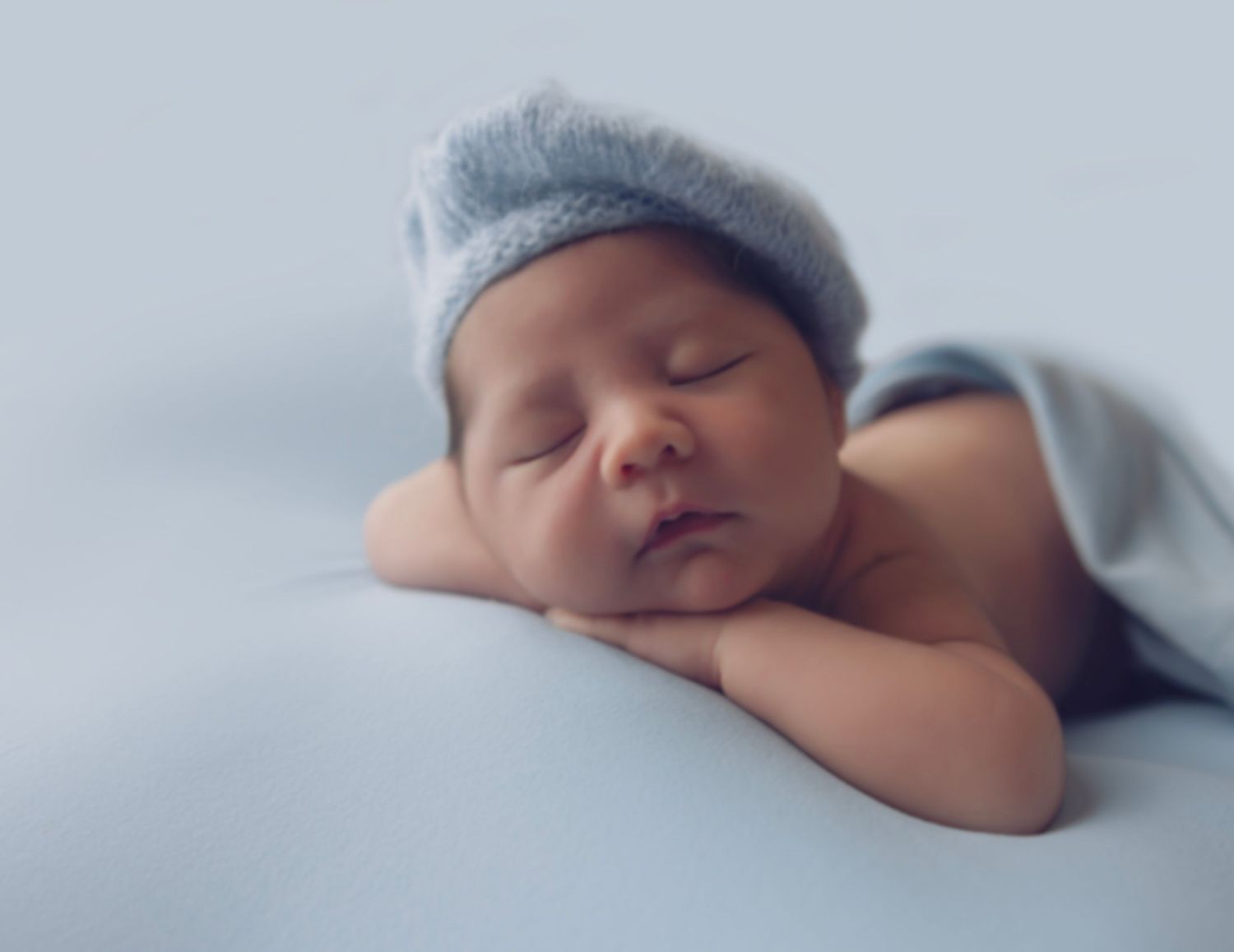 Peaceful sleeping newborn baby wearing soft gray hat rests head on folded arms in dreamy portrait.