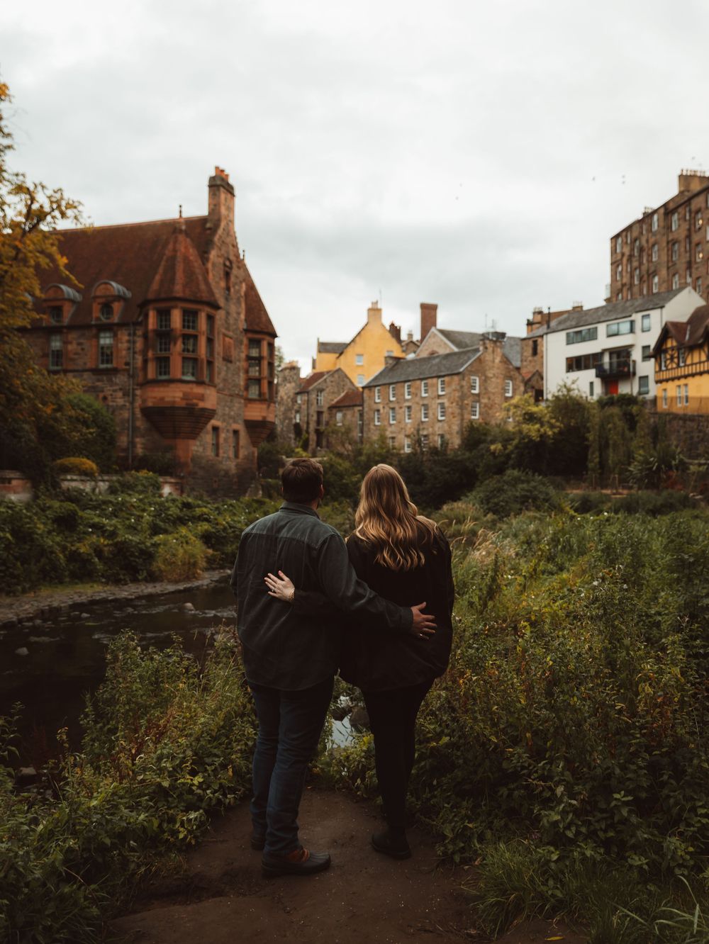 Couple walking along stone path with historic Edinburgh buildings in background.
