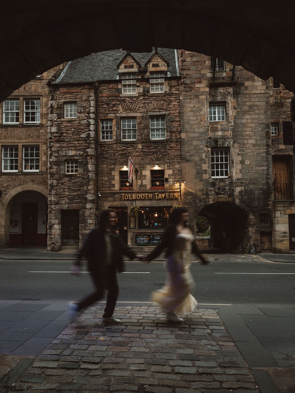 Motion-blurred figures walking across historic cobblestone square at dusk.