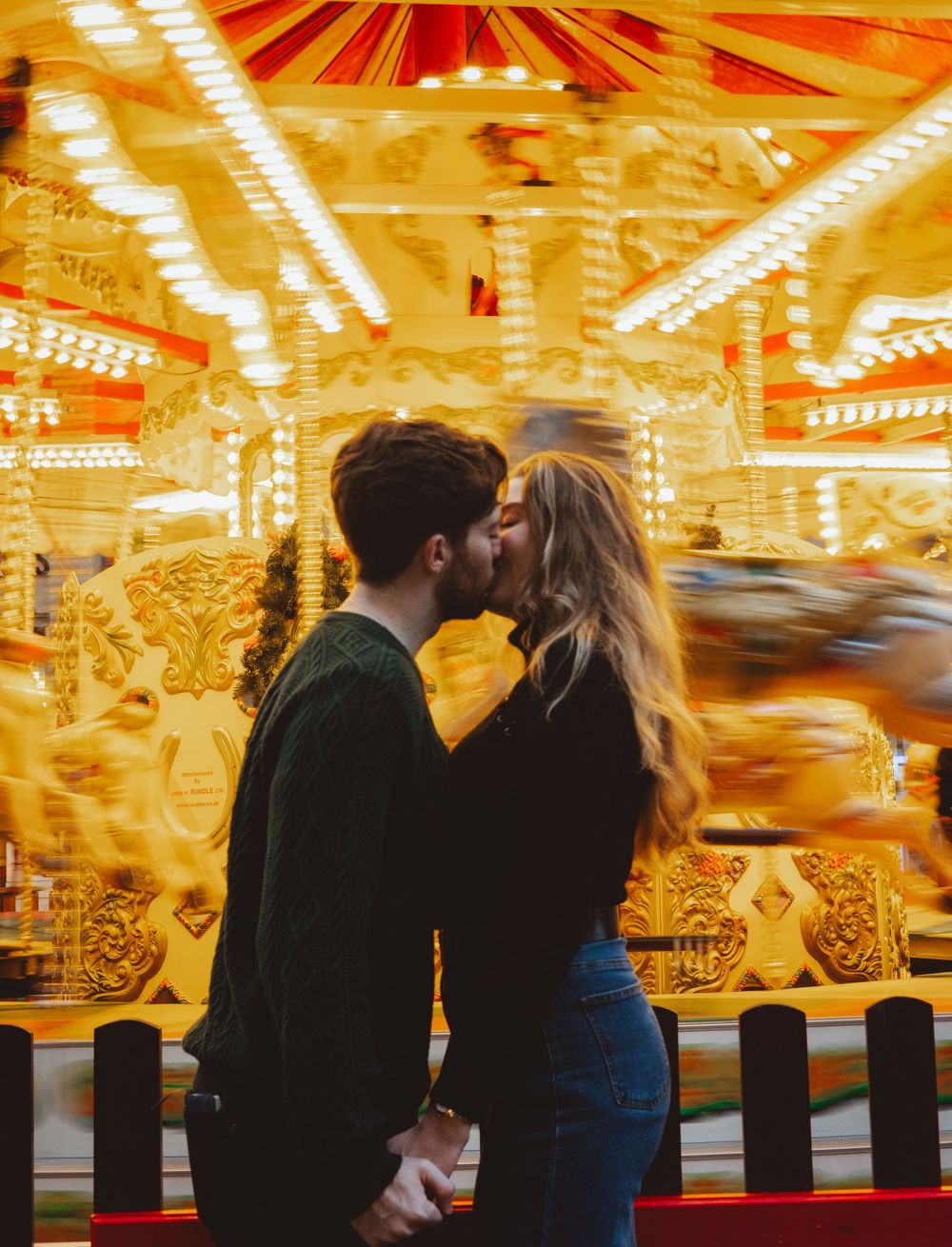 Carousel lights create golden bokeh effect at night with silhouettes in foreground.