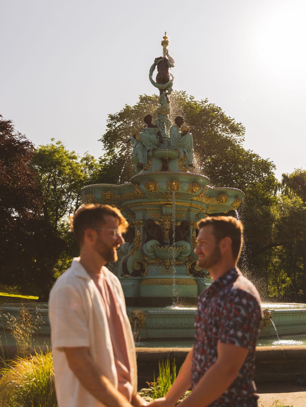 Golden sunset light illuminates ornate fountain in public garden.