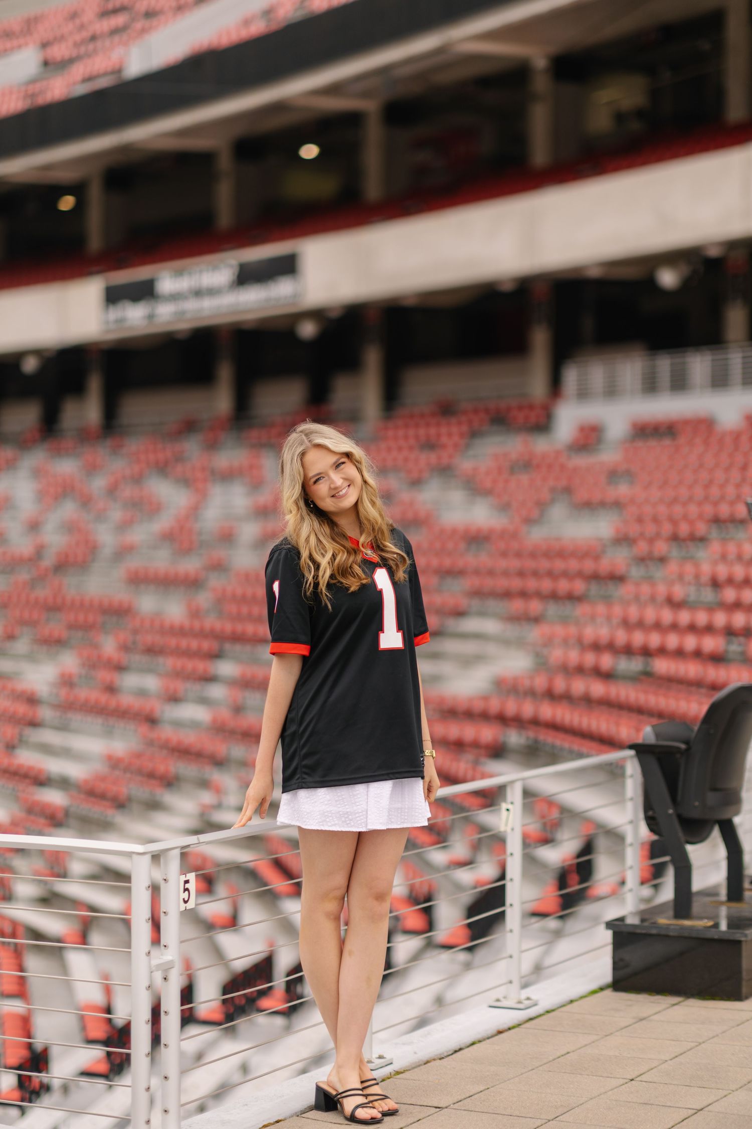 A person wearing a black floral dress with puff sleeves poses outdoors near bleachers during golden hour.