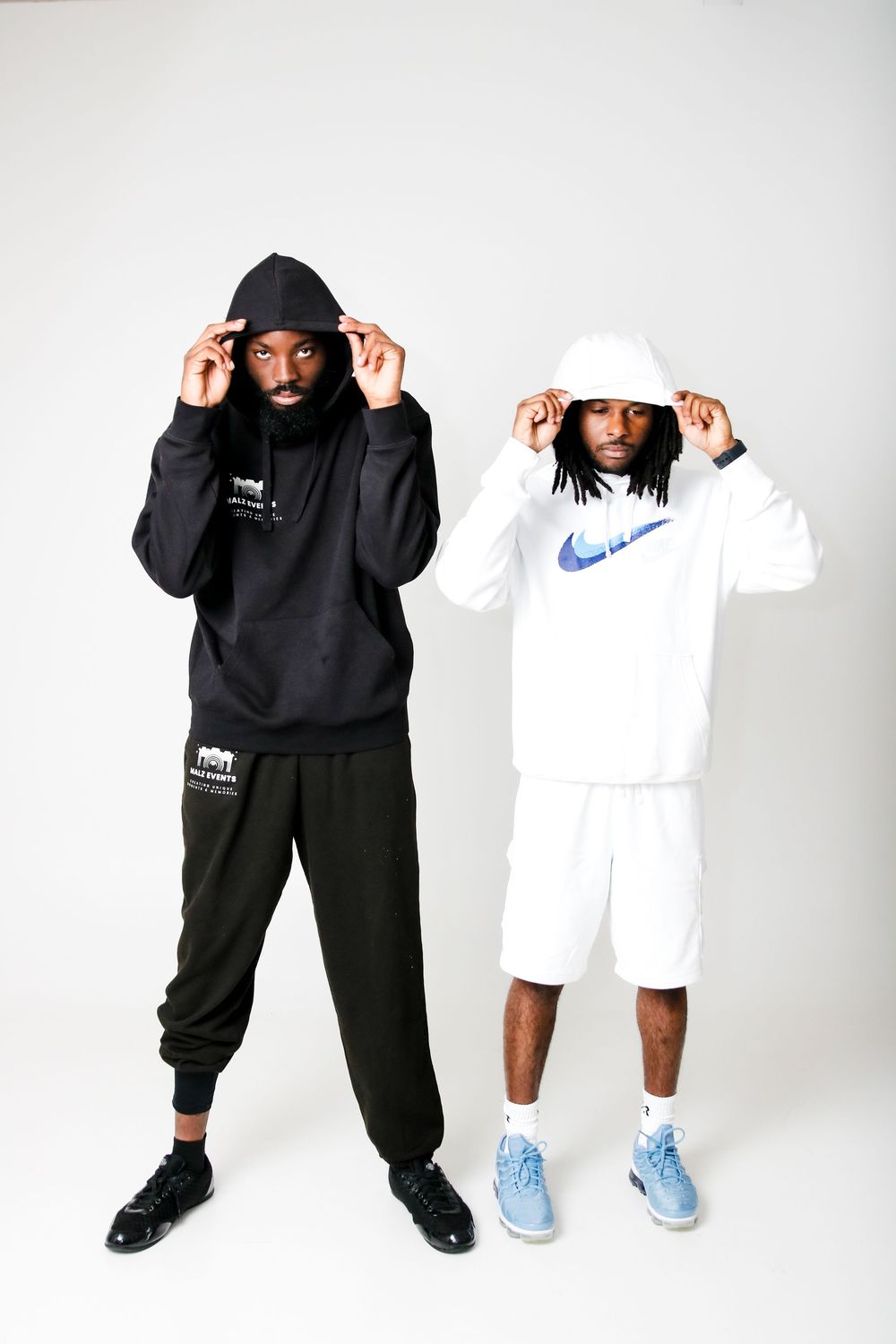 Two people in matching Nike hoodies, one black and one white, pose with hands on their hoods.