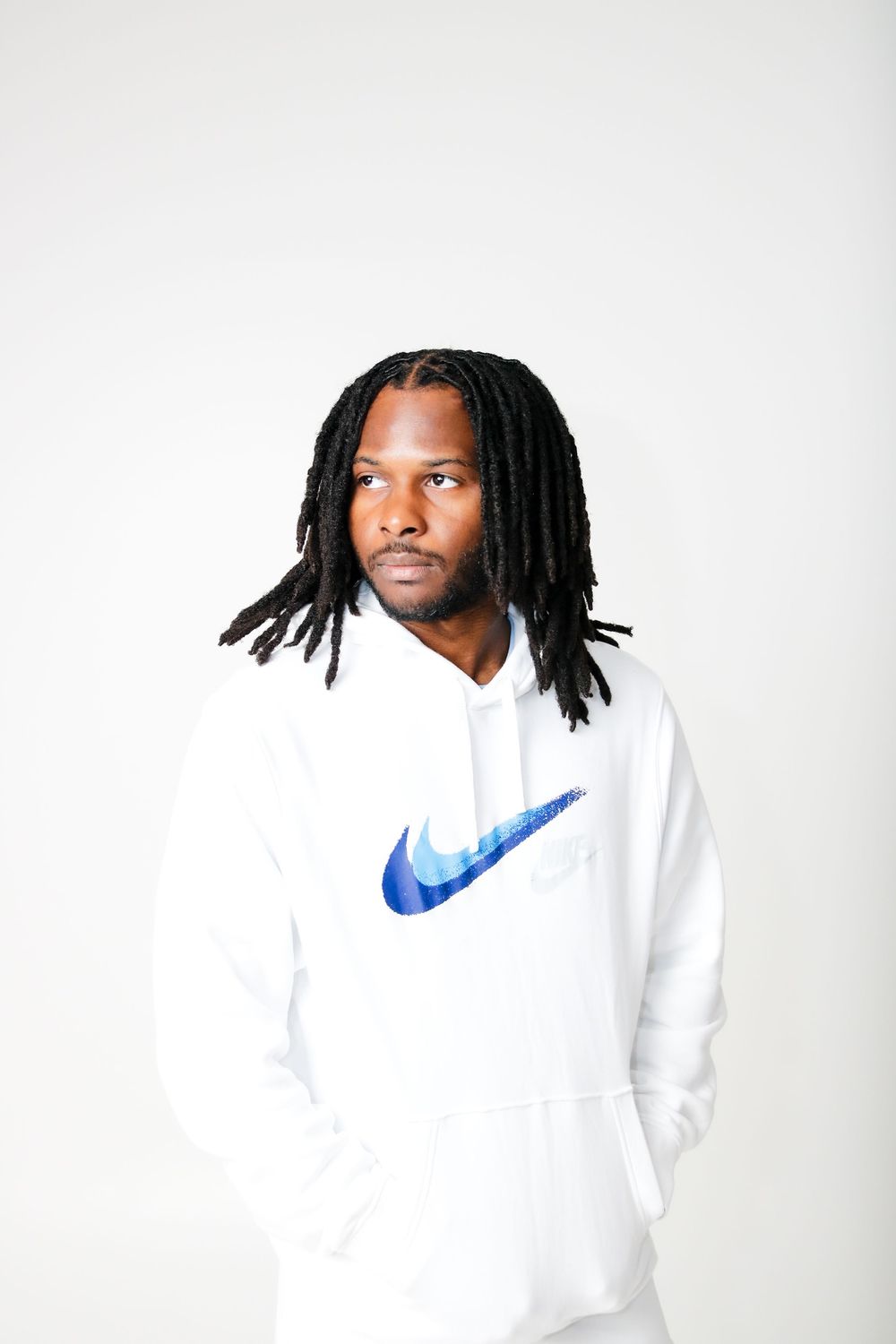 Person in white Nike hoodie with locs poses against white background.