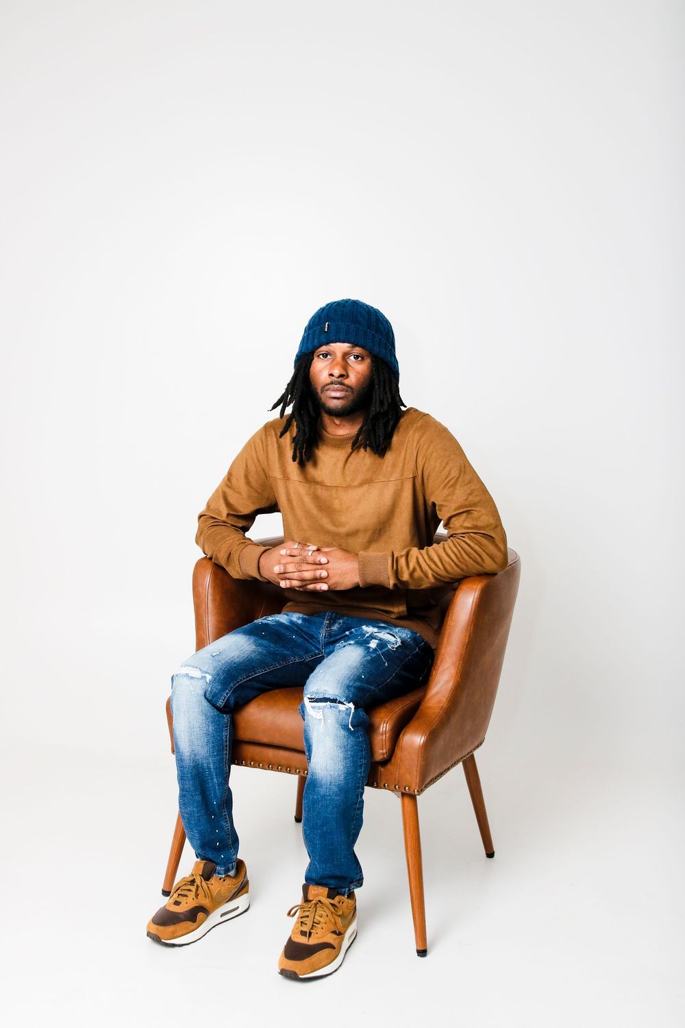 Person in casual attire sits in brown leather chair wearing blue beanie and distressed jeans.