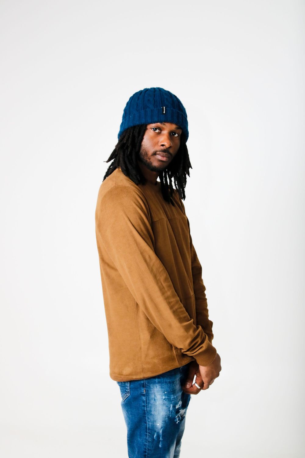 Person wearing blue beanie and tan sweater poses against white backdrop.
