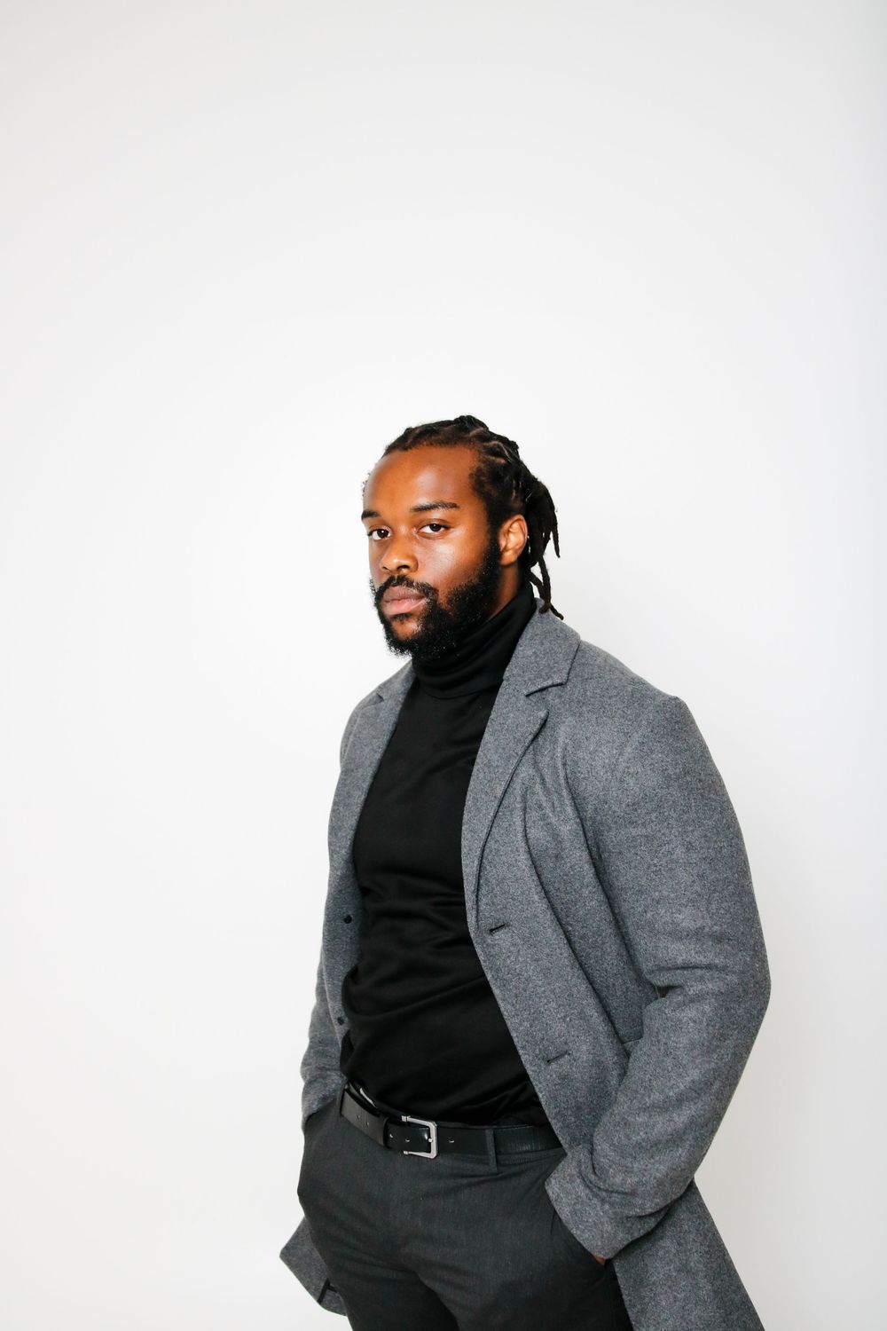 Person in grey coat and black turtleneck poses professionally against white background.