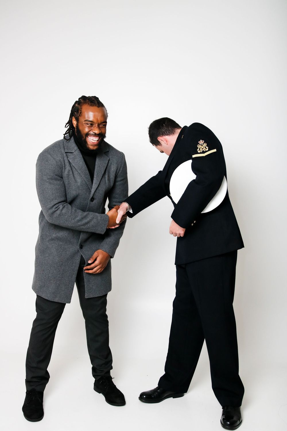 Two people shake hands and laugh together against white background.