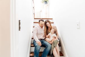 Family sitting together on white wooden stairs in a bright, minimalist home interior.
