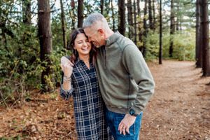 A couple sharing a joyful moment while walking on a forest trail surrounded by tall pine trees.