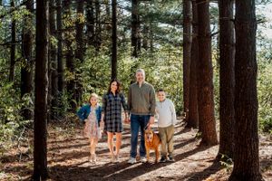 A group walks together on a forest trail among tall pine trees on a sunny afternoon.