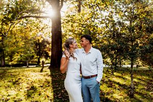 Golden sunlight streams through autumn trees as couple poses in outdoor engagement session.