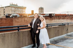 A couple in wedding attire shares a romantic moment on a rooftop with city buildings in the background.