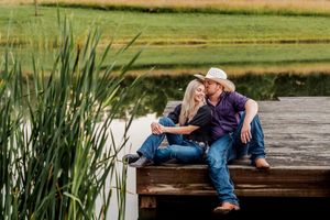 A romantic photoshoot in a rustic outdoor setting with a wooden dock and tall grass at sunset.