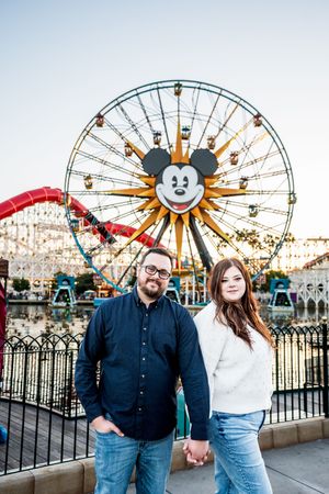 A couple poses in front of Mickey's Fun Wheel at Disney California Adventure during sunset.
