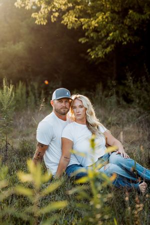 Couple relaxes together in a sunlit meadow with wildflowers and natural scenery during golden hour.