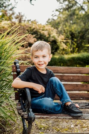 A child sits on a wooden park bench surrounded by fall foliage and ornamental grasses.