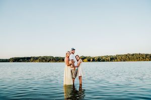 A couple stands on a wooden dock overlooking a peaceful lake during a sunny summer day.