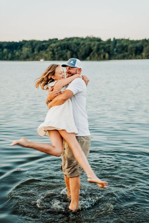 A joyful pair playing together and splashing in a tranquil lake surrounded by trees in an intimate summer moment.