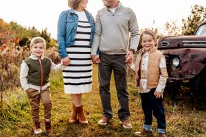 A family stands together in a fall field beside a vintage rusty truck during golden hour.