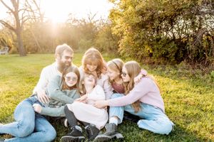 A joyful family sits together on a blanket in a sunny park during golden hour in autumn.