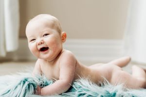 Happy laughing baby lying on soft teal furry blanket showing pure joy during photography session.